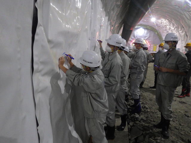 トンネルの防水シートに現場見学記念のメッセージを書込む黒沢尻工業高校の生徒たちの写真
