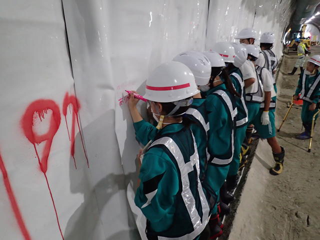 トンネルの防水シートに現場見学記念のメッセージを書込む金ヶ崎中学校の生徒たちの写真