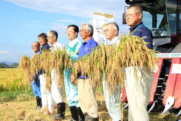 収穫した稲穂を手にもって、秋の実りを実感する生産者と知事