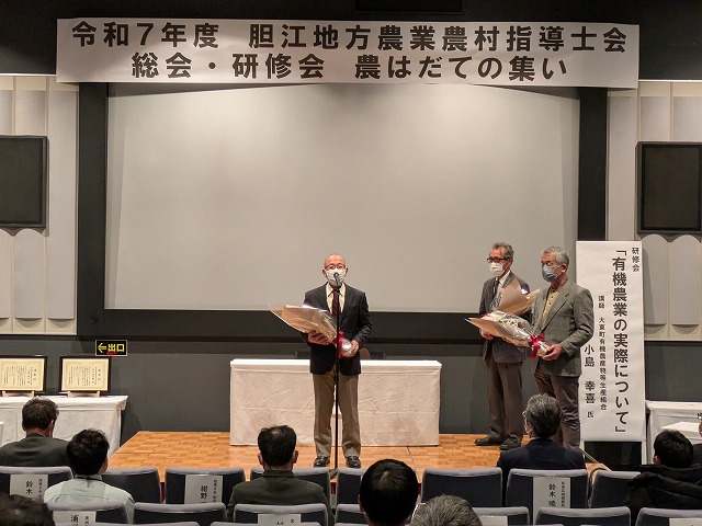 認定期間を満了した指導士が花束を受け取り、会場からは感謝の拍手が送られている。