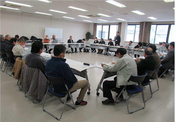 多くの出席者が一堂に会し、机を囲んでいる様子。